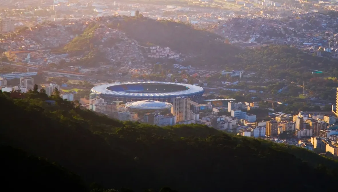 Estádio visto de longe, com a cidade e o pôr do sol ao fundo
